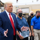 President Donald Trump speaks to the press as he tours an area affected by civil unrest in Kenosha, Wisconsin on September 1, 2020, as John Rode, center, the former owner of the building that contained Rode’s Camera Shop looks on holding a sign.